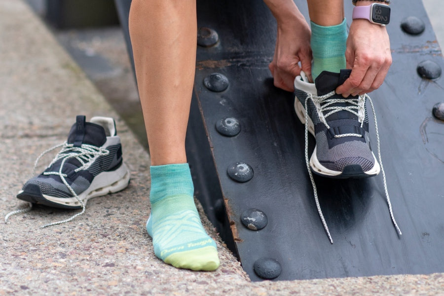 A runner putting her foot into running shoes while wearing teal no cushion run quarters