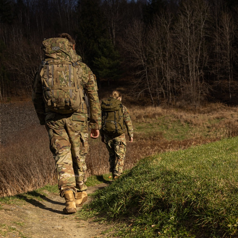 Two people in military uniform hiking across grassy terrain