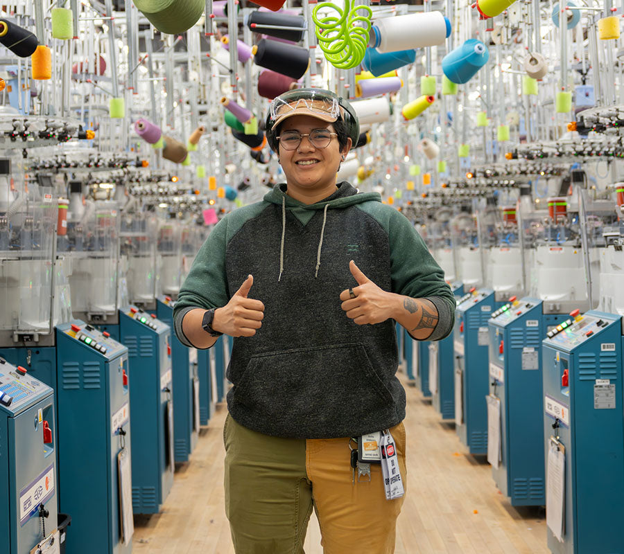 Anita holding two thumbs up and smiling standing at the Darn Tough knitting mill