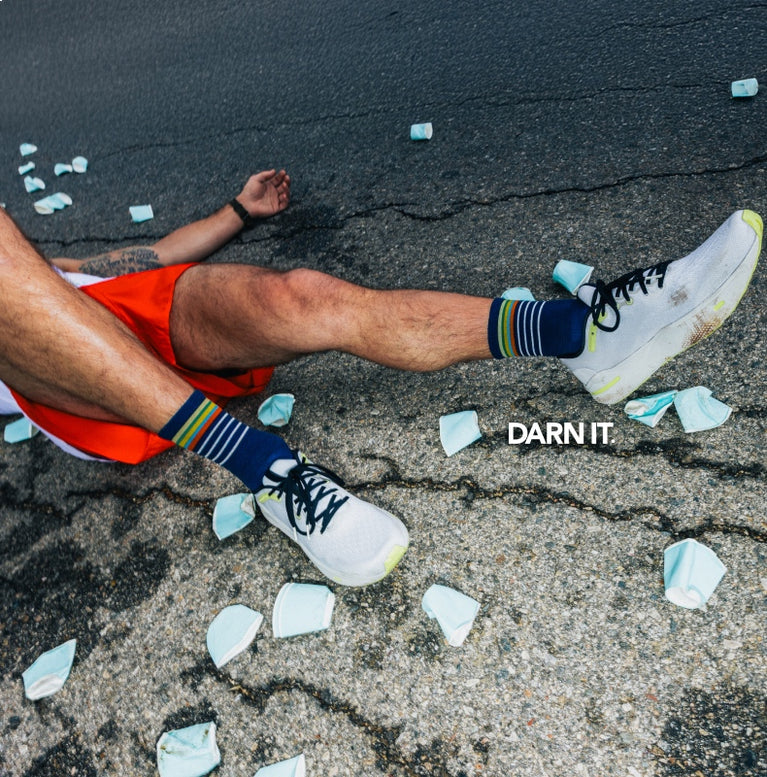 A marathon runner wearing Darn Tough run socks; he's collapsed on the ground with water cups all around him. 