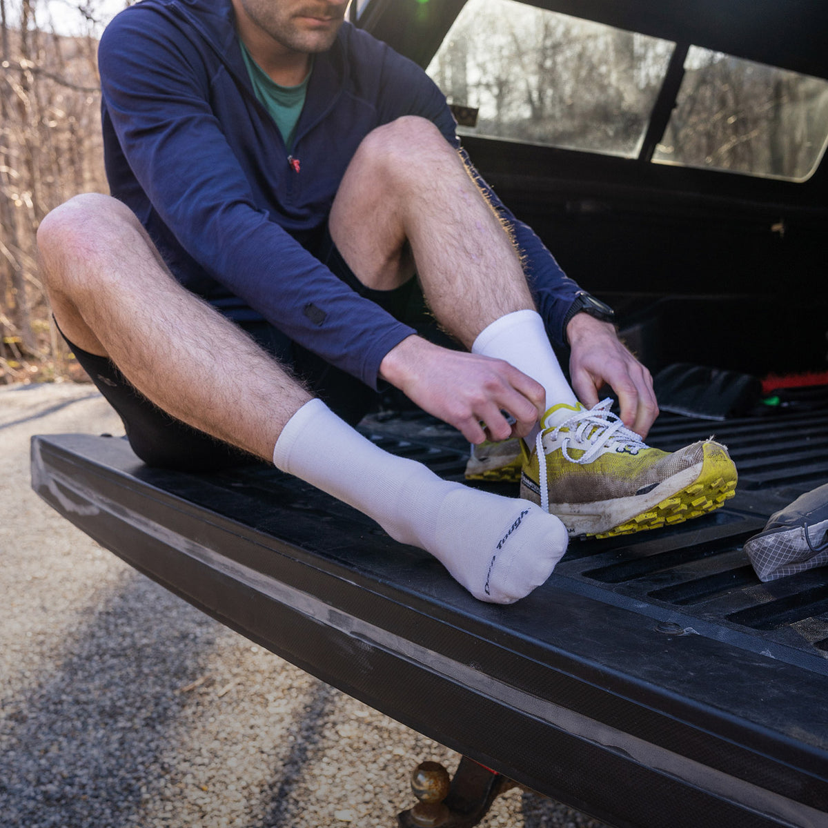 A runner seated to put on their shoes wearing men's run micro crew socks in solid white