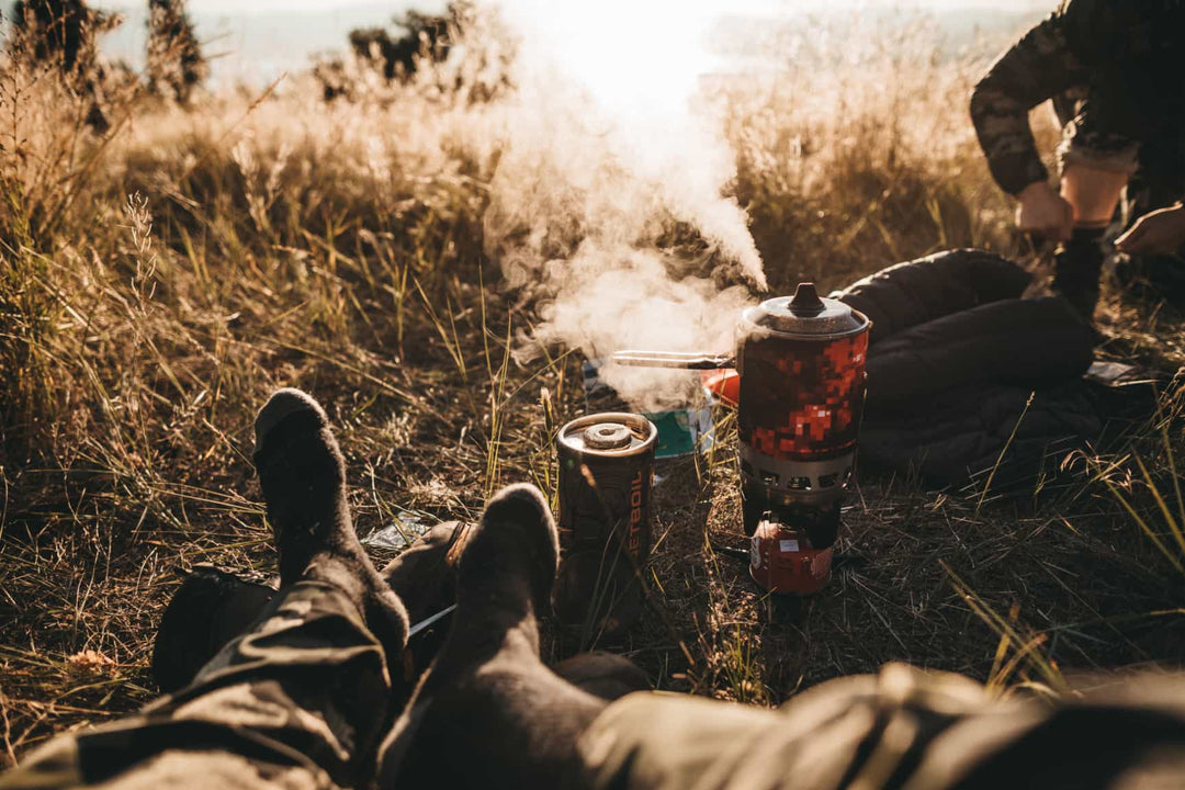 Shot of model in a field wearing hunting socks with feet propped up by steaming camp stove.