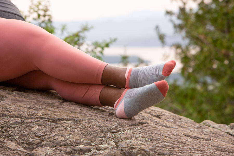 A woman running sitting on a rock wearing no show running socks in pink and gray