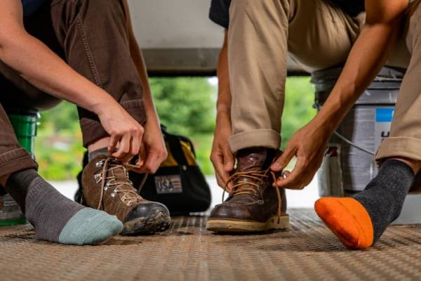 Two workers pulling on steel toe boots over darn tough steely steel toe socks