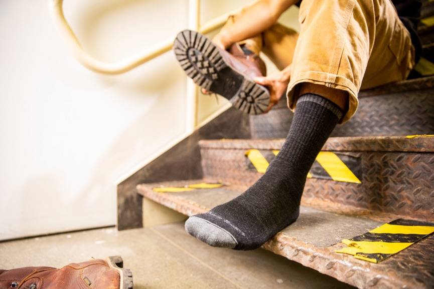 Construction worker pulling off boots wearing darn tough heavy duty work socks