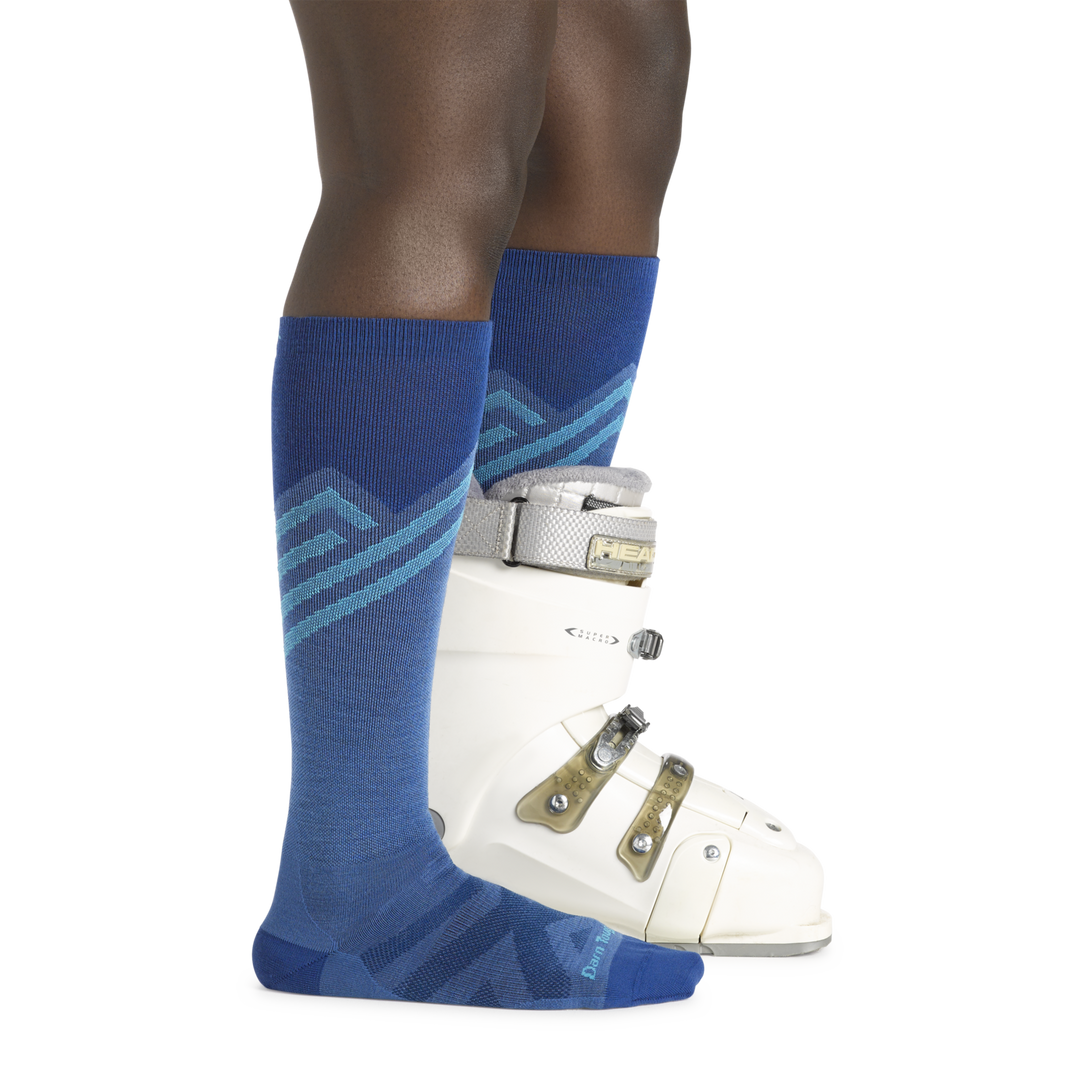Woman wearing Women's Peaks Over-the-Calf Ultra-Ligtweight Ski and Snowbaord socks in stellar blue with a ski boot