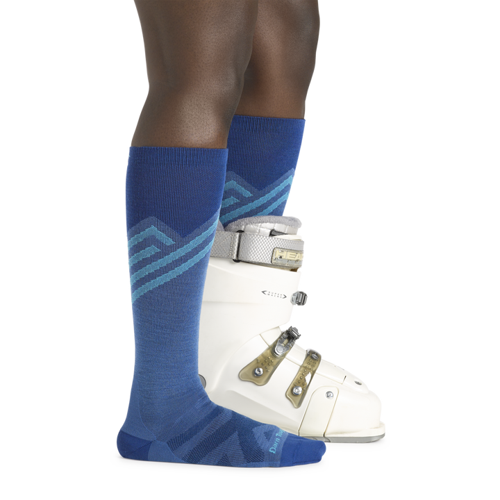 Woman wearing Women's Peaks Over-the-Calf Ultra-Ligtweight Ski and Snowbaord socks in stellar blue with a ski boot