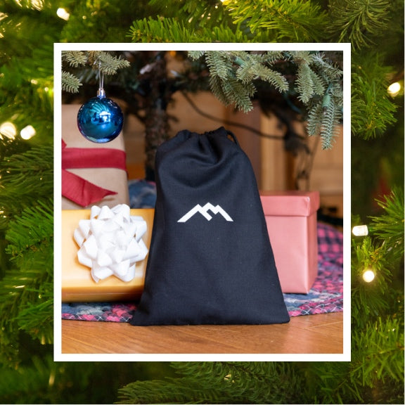 A black cloth bag with the Darn Tough mountain logo on it, full of socks and under a tree