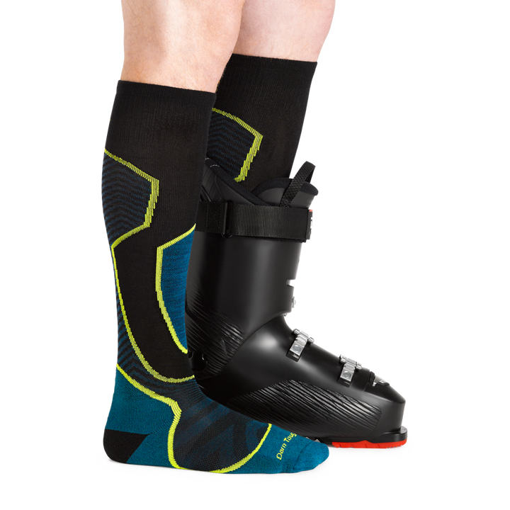 Close up of Men's Outer Limit Over-the-Calf Lightweight Ski and Snowboard Sock in blue, black and green with a ski boot