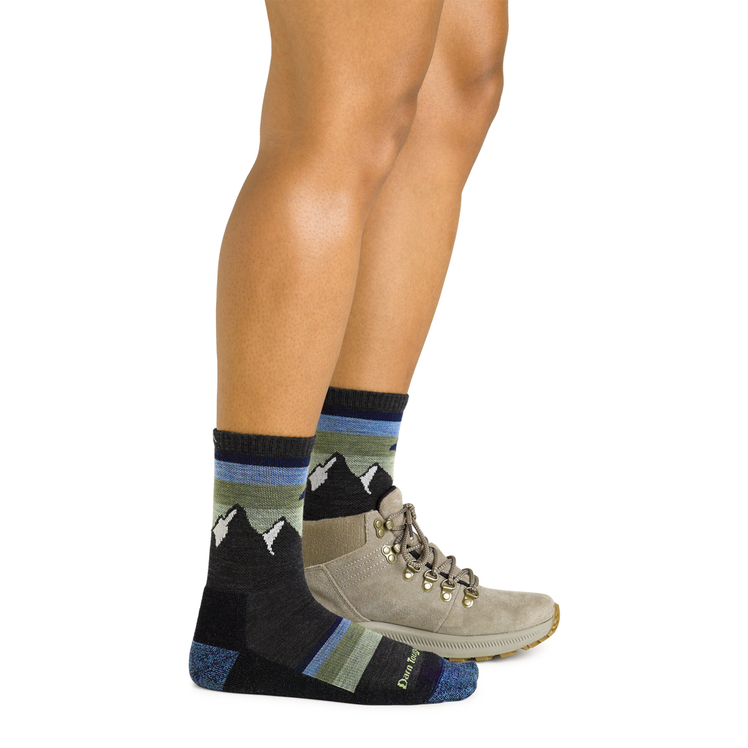 Side studio shot of model wearing women's sunset ledge micro crew hiking sock in charcoal with brown hiking shoe on left foot