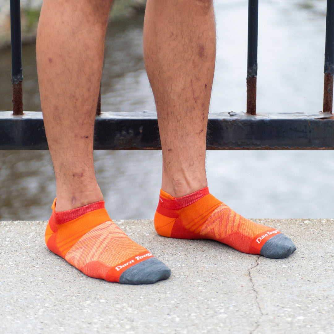 Runner standing on a bridge wearing 1033 no show running socks in lava orange