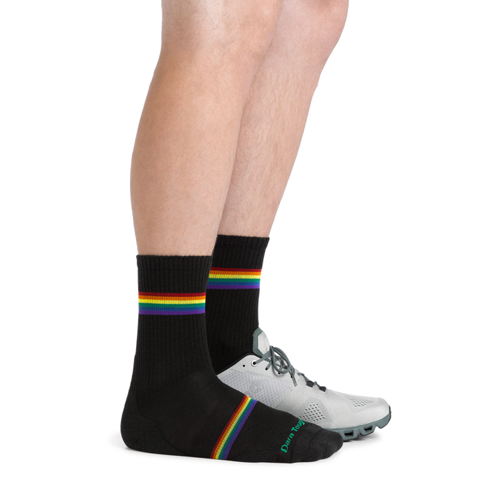 Man standing wearing Men's Prism Micro Crew Lightweight Running Sock with rainbow stripes and a running shoe on one foot