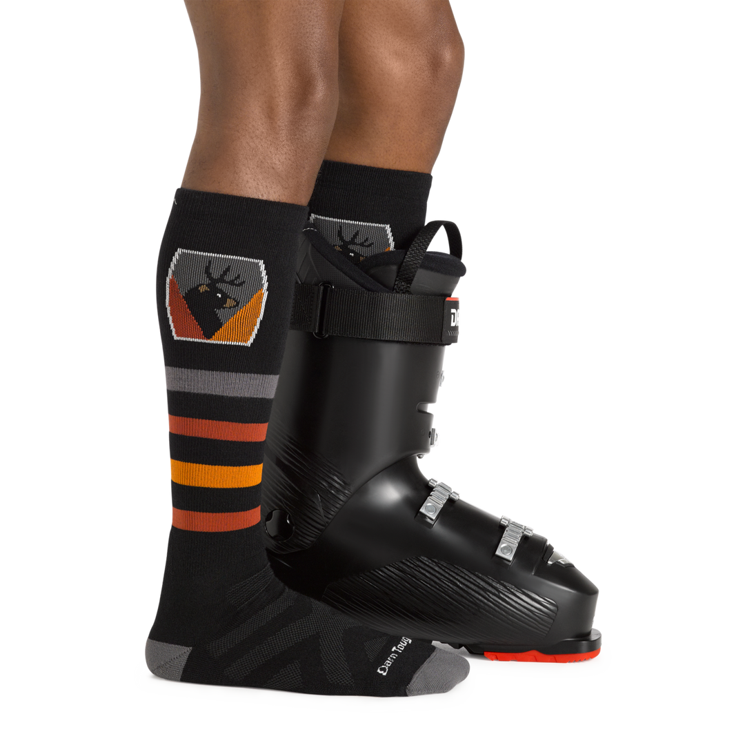 Men's thermolite beer (deer and bear) badge over the calf Ski and Snowboard sock in black with ski boot on left foot