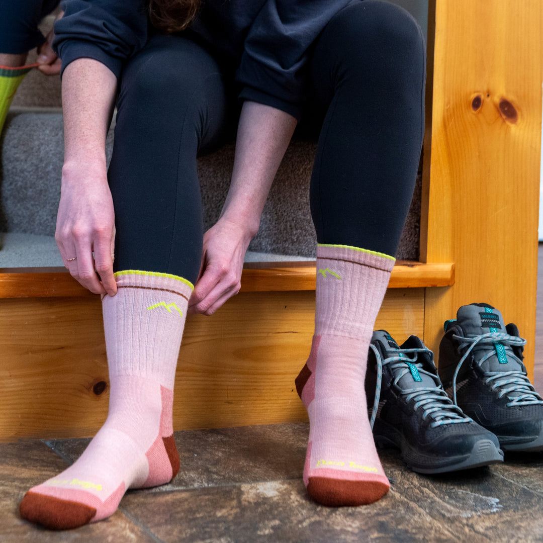 Woman sitting down putting on Micro Crew Hiking socks in pink with red and yellow accents