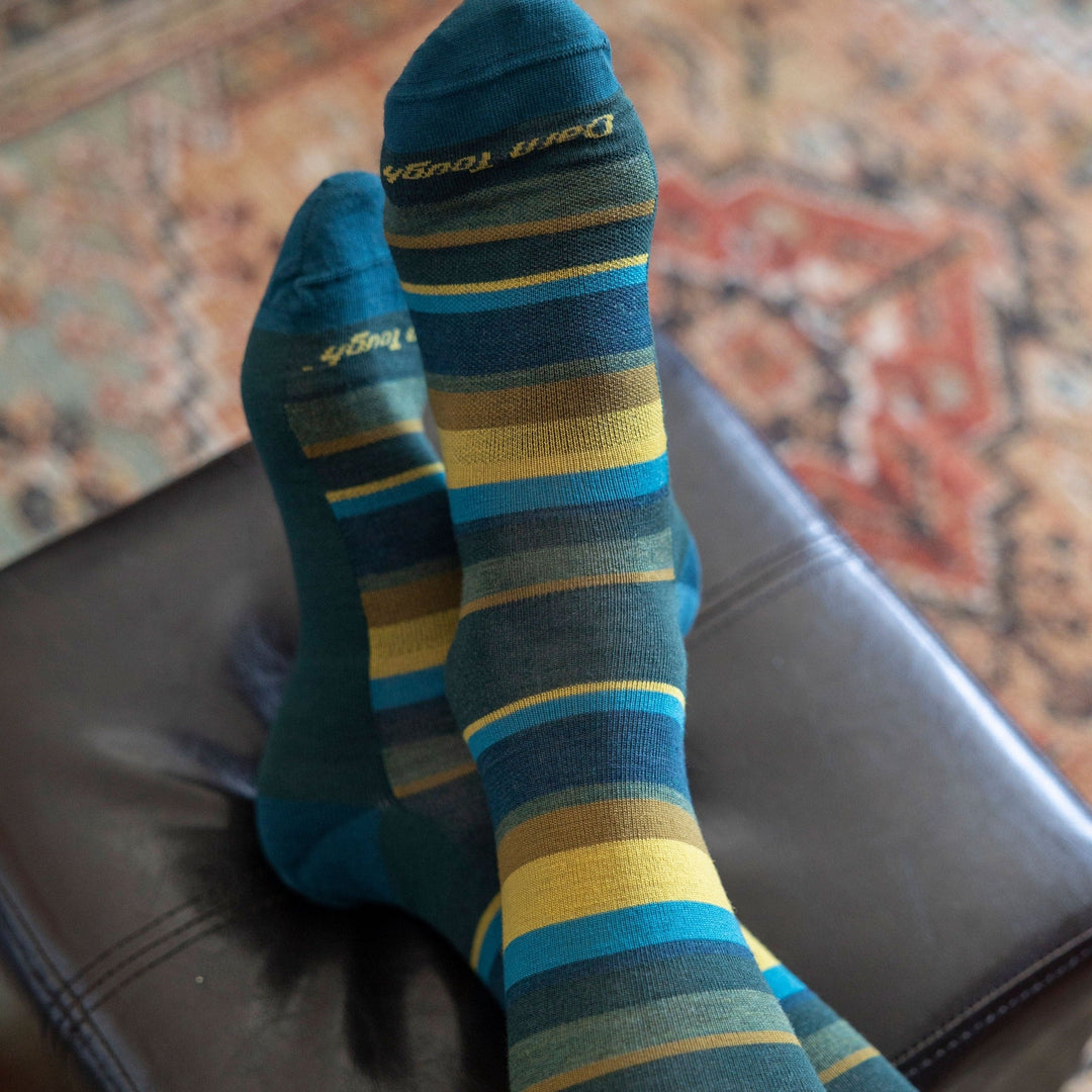 Close up shot of model laying on a brown leather couch wearing men's druid crew lifestyle sock in bottle blue