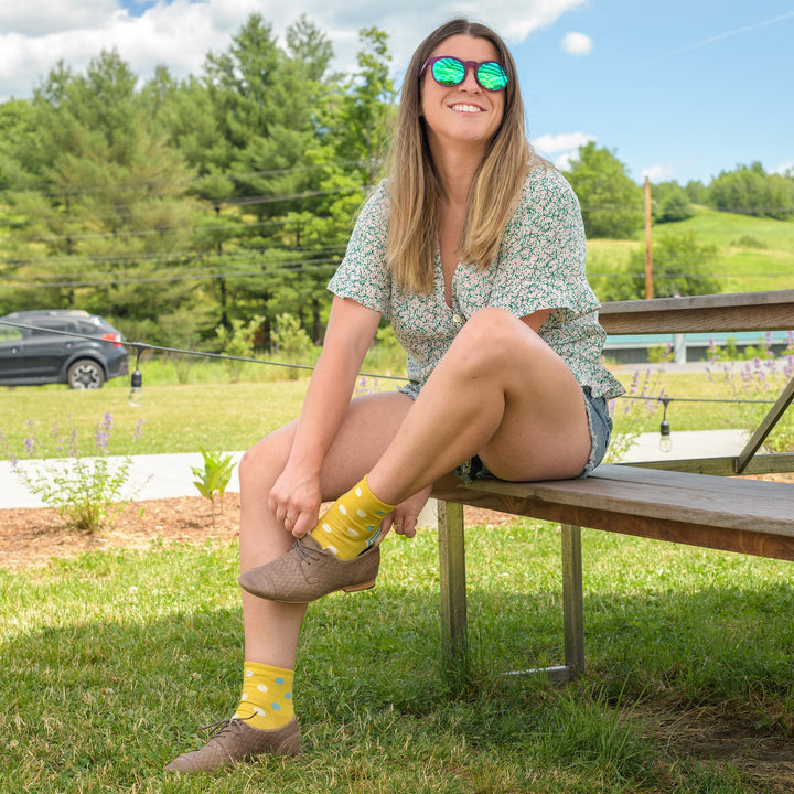 Full shot of model sitting at a picnic bench wearing the women's dottie shorty lifestyle socks in buttercup yellow