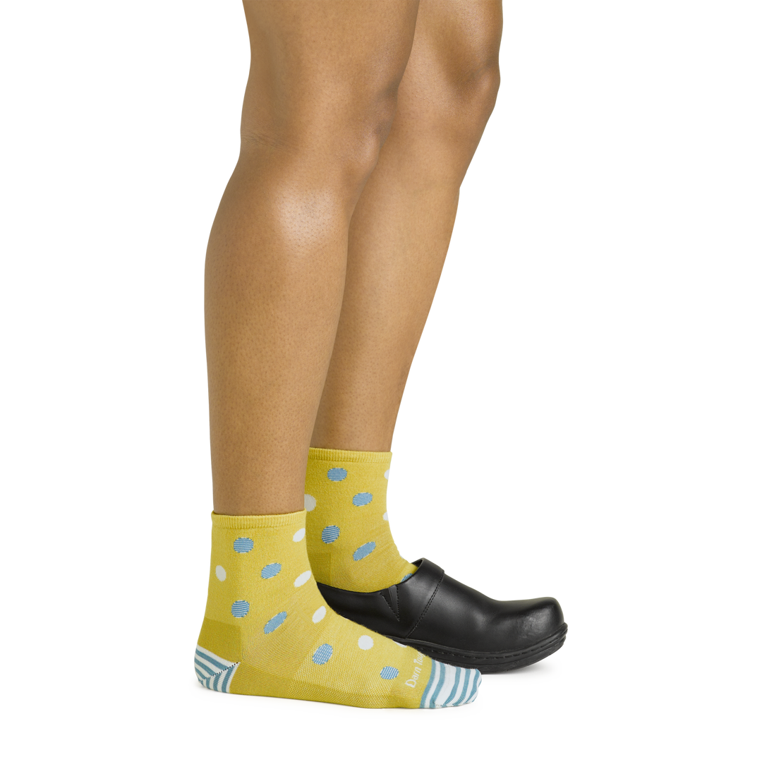 Side shot of model wearing the women's dottie shorty lifestyle socks in buttercup yellow with a black shoe on her left foot