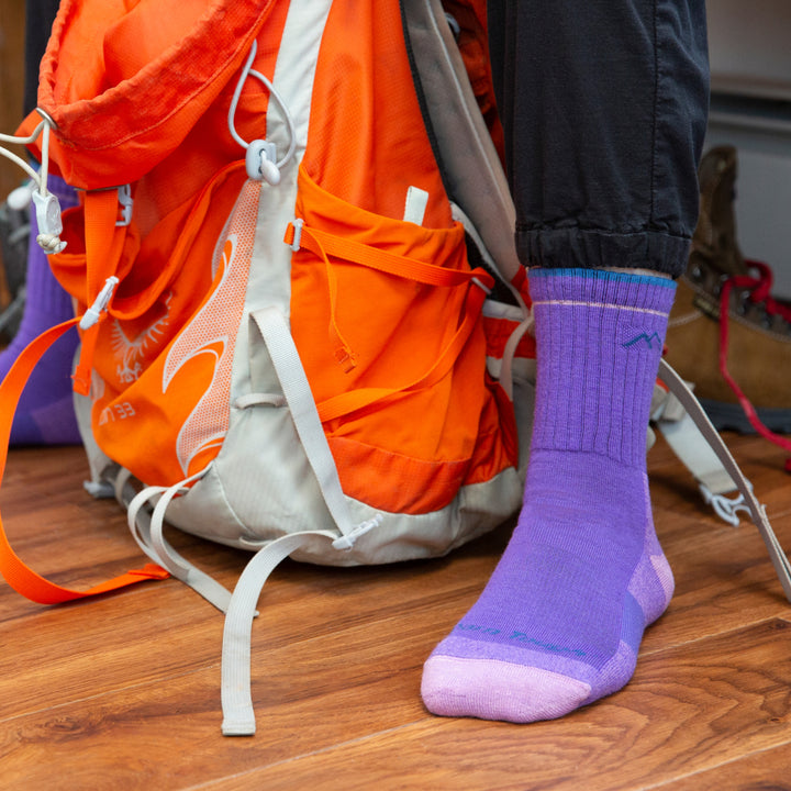 Model sitting with hiking backpack wearing purple micro crew hiking socks