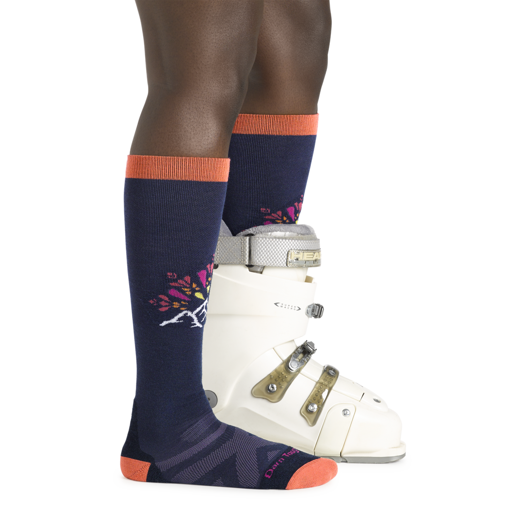 Model wearing Women's Daybreak Over-the-Calf Ski and Snowboard Socks in Navy and orange with mountain graphic and a boot