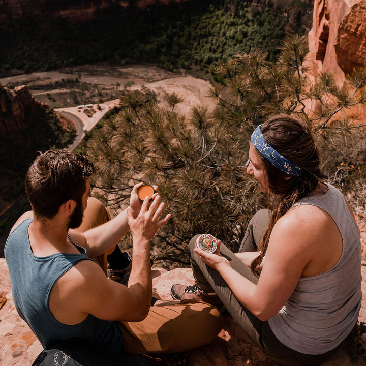 model image of two people sitting on rock edge applying the sore muscle rub