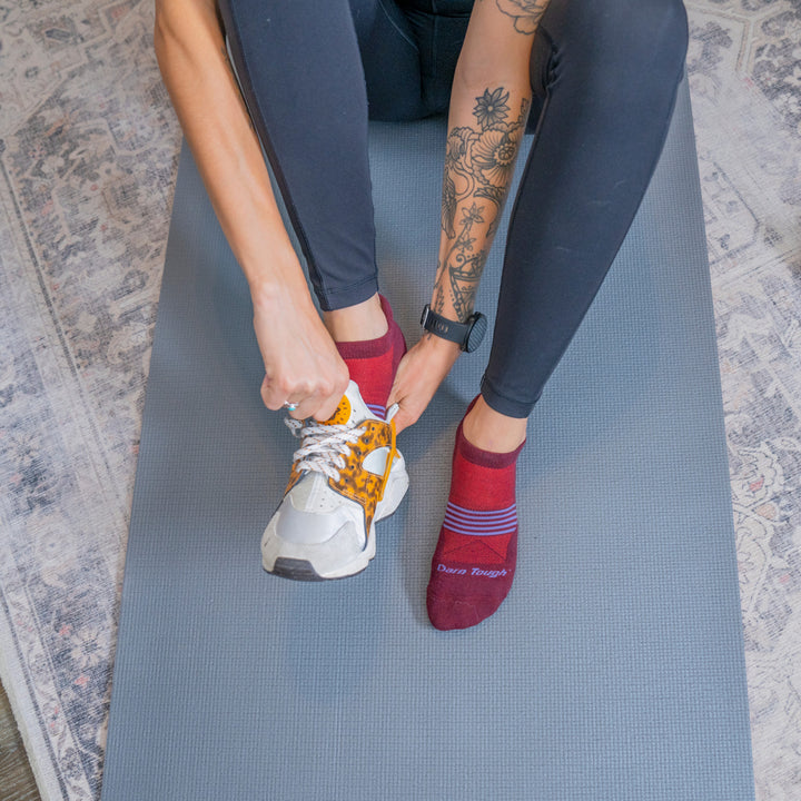 Model sitting on yoga mat putting on sneakers wearing the 1112 Element no show in burgundy 