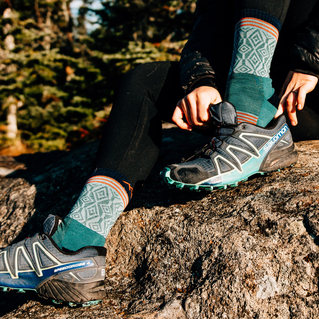 Close up lifestyle shot of woman putting her trail runners on while wearing her Sobo's in Teal and black leggings.