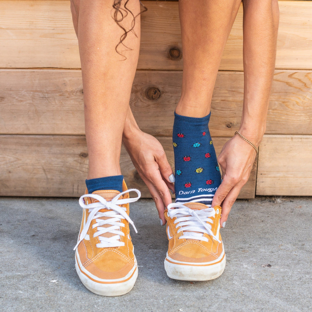 Closeup of woman putting low top sneakers on over lucky lady fun ladybug socks in blue