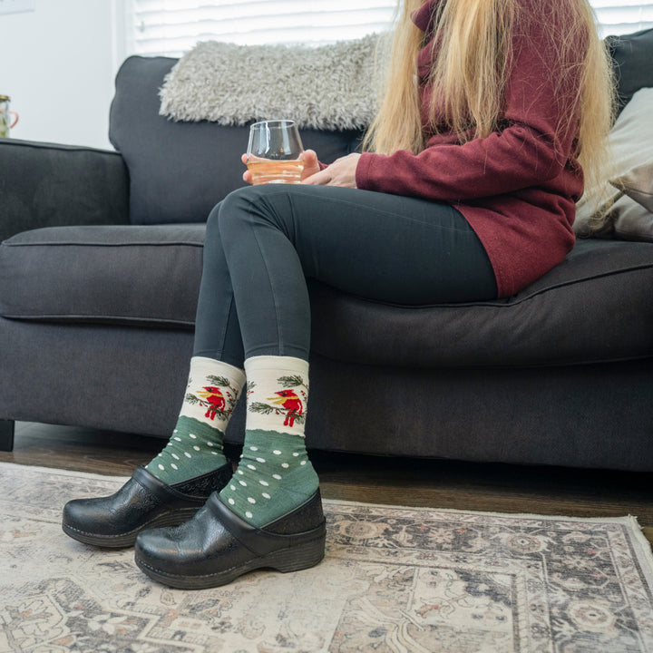 Women sitting on a couch  wearing the 6209 Wildlife in evergreen , featuring the green body and white dot with cardinal image on the ankle