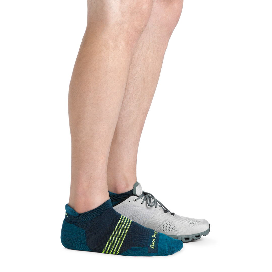 Man wearing Element No Show Tab Lightweight Running Sock in Blue with lime Green stripes and a running shoe on back foot