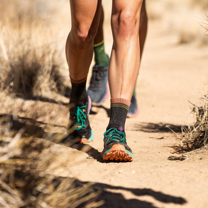 Lifestyle shot of woman walking in the desert wearing her Sobo socks in Charcoal with teal and orange trail runners.