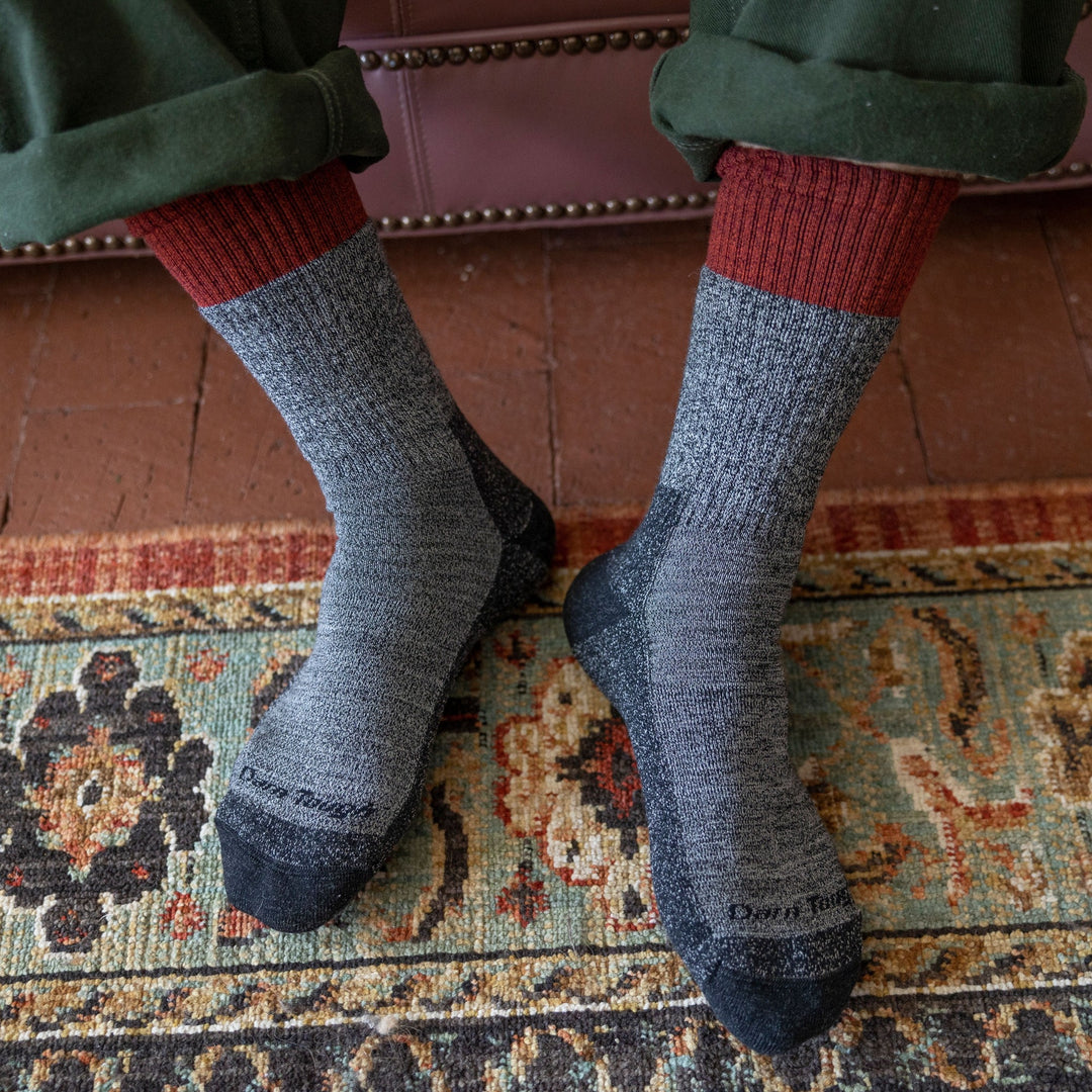 Close up overhead shot of model wearing men's scout boot hiking sock in pepper gray with patterned rug in the background