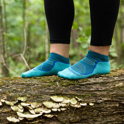 Close up shot of model standing on a log in the woods wearing the women's no show hiking sock in cascade