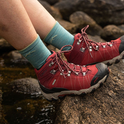 Close up shot of model sitting on a rock on trail wearing red hiking shoes and the women's light hiker micro crew hiking sock in aqua