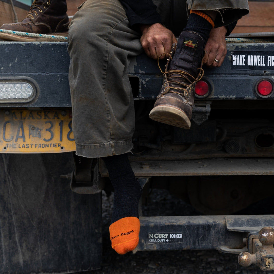Model sitting on the back of a truck wearing men's 2006 steely boot work sock in graphite while putting on work boots