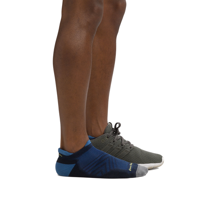 Side shot of model wearing the men's run no show tab running sock in eclipse blue with a gray sneaker on his left foot