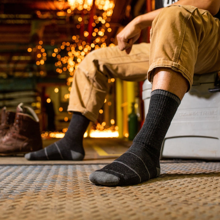 Close up shot of model sitting on a cooler wearing the men's william jarvis boot work sock in gravel