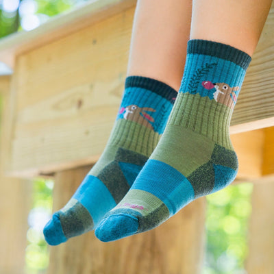 Close up shot of a model sitting on wood railing with their feet hanging off wearing the kids' bubble bunny jr. micro crew hiking sock