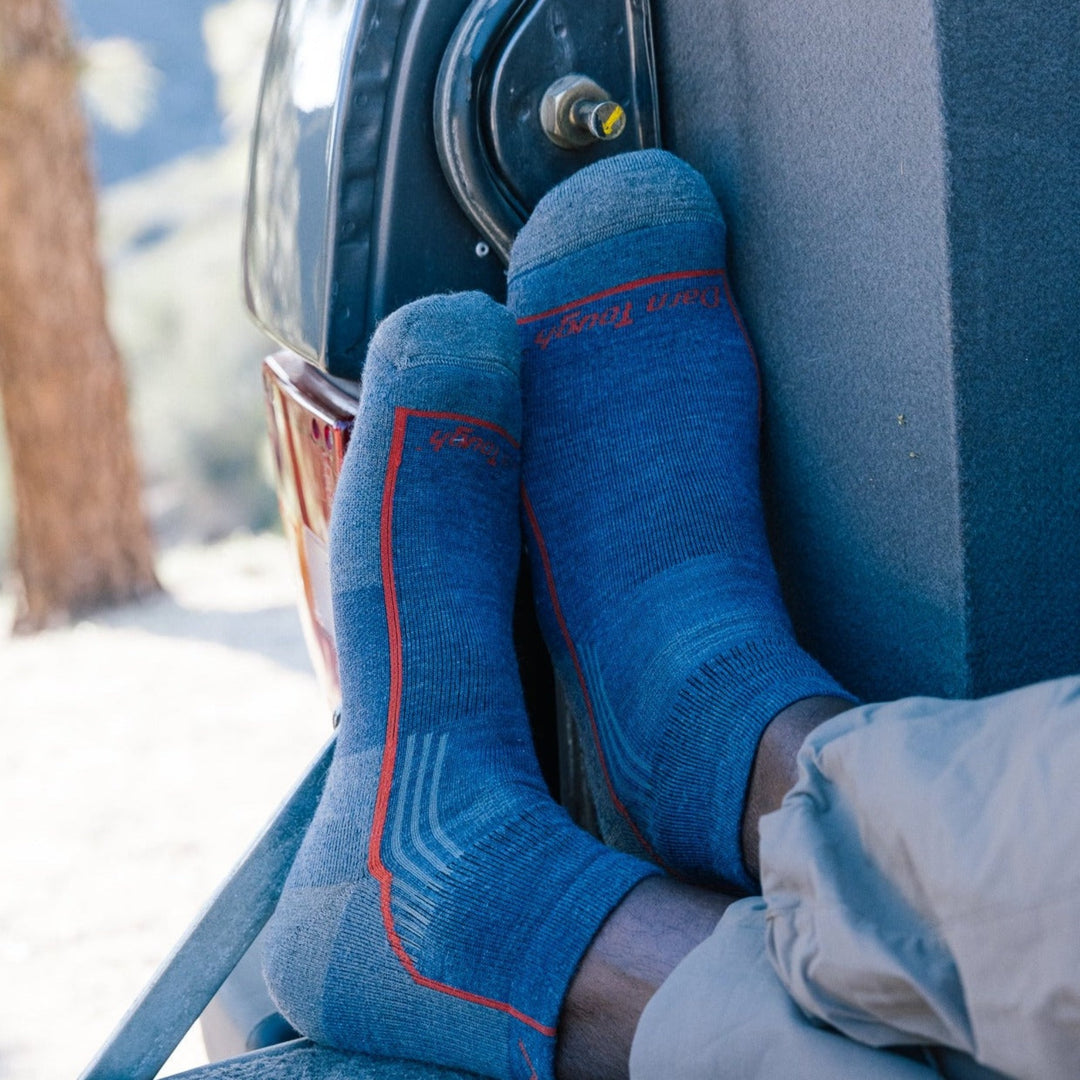 Close up shot of model sitting on the back of a truck wearing the men's quarter hiking sock in denim blue