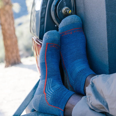 Close up shot of model sitting on the back of a truck wearing the men's quarter hiking sock in denim blue