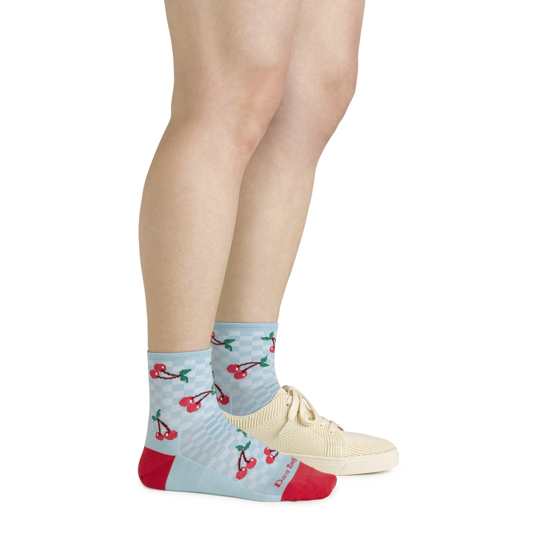 Side shot of model wearing the women's fruit stand shorty lfiestyle socks in glacier blue with a white shoe on her left foot