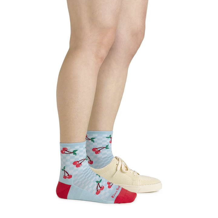 Side shot of model wearing the women's fruit stand shorty lfiestyle socks in glacier blue with a white shoe on her left foot