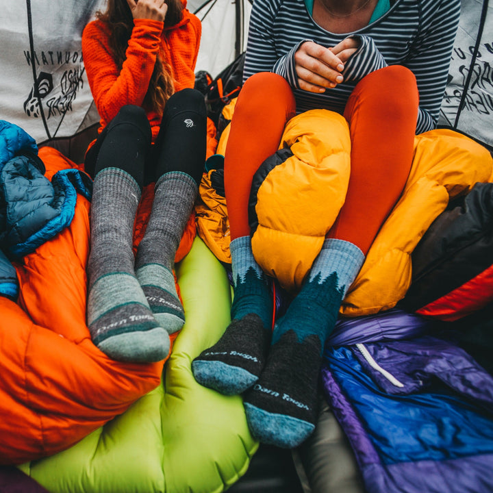 Close up shot of 2 models sitting in a tent, one wearing the women's boot hiking sock in slate and the other wearing the women's treeline micro crew hiking sock in blue