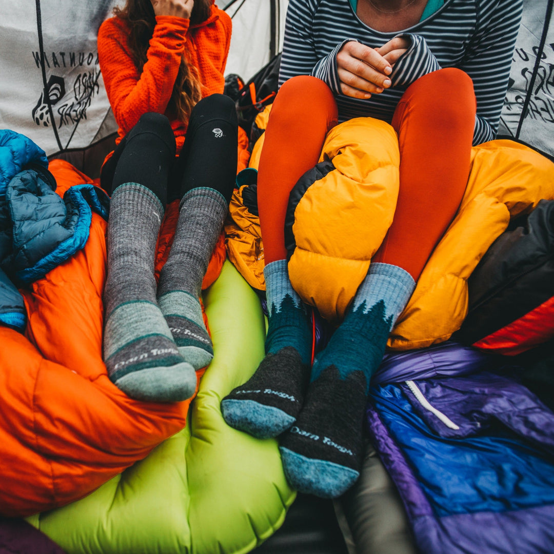 Close up shot of models sitting inside of a tent wearing the women's treeline micro crew hiking sock in blue and the women's boot hiking sock in slate