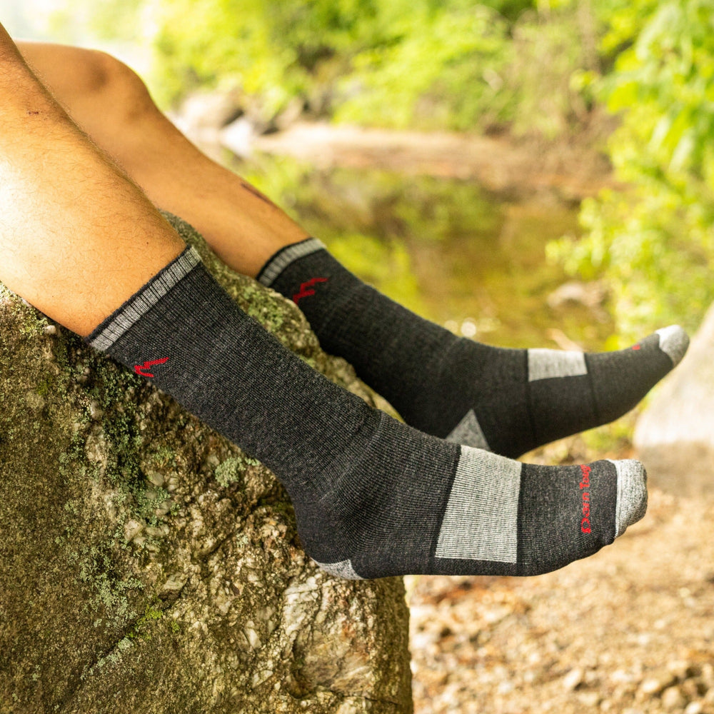 Close up shot of model sitting on a rock wearing the men's boot hiking sock in black