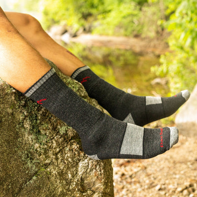 Close up shot of model sitting on a rock wearing the men's boot hiking sock in black