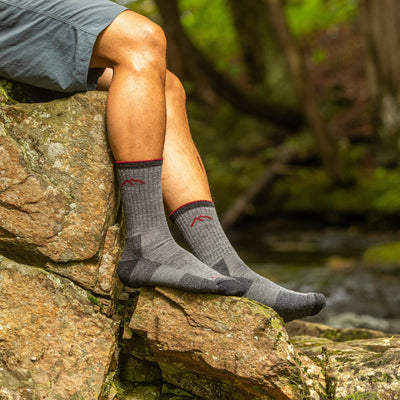 Model sitting on a river rock with no shoes wearing men's micro crew hiking sock in charcoal 