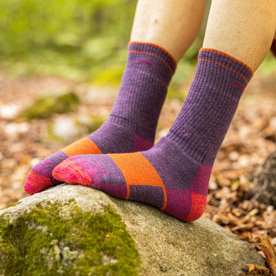 Close up shot of model sitting on a rock wearing the women's boot hiking sock in plum heather