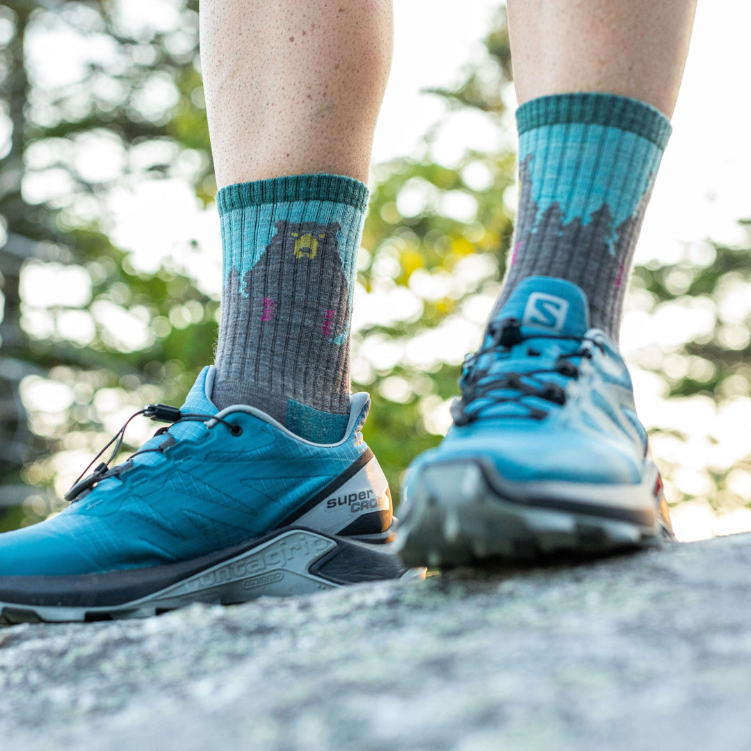Close up shot of model standing on a rock wearing the women's bear town micro crew hiking sock in the color aqua with blue hiking shoes