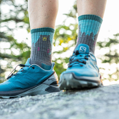 Close up shot of model standing on a rock wearing the women's bear town micro crew hiking sock in aqua with blue hiking shoes