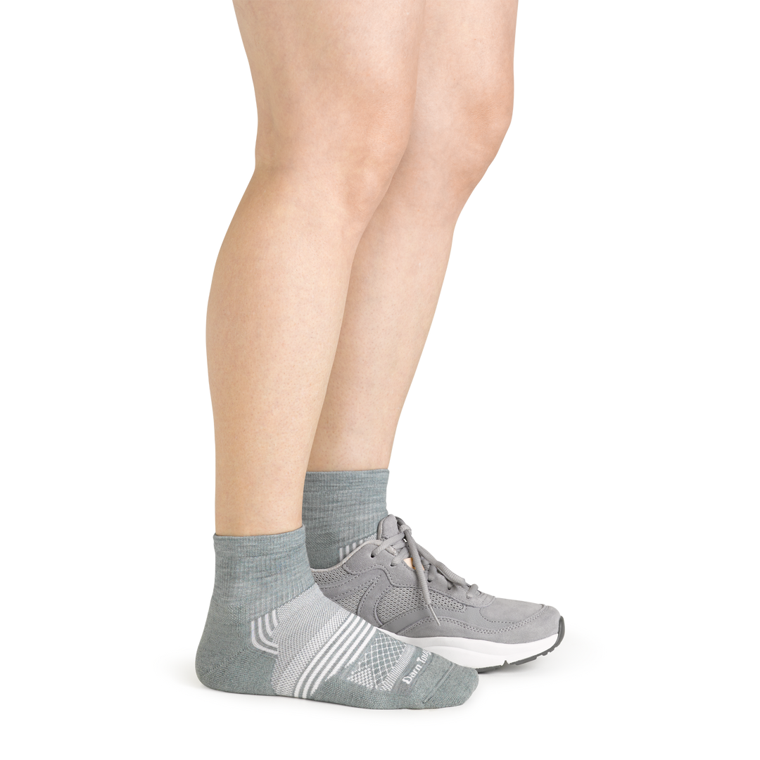 Side studio shot of model wearing women's element quarter athletic sock in seafoam green with gray sneaker on left foot